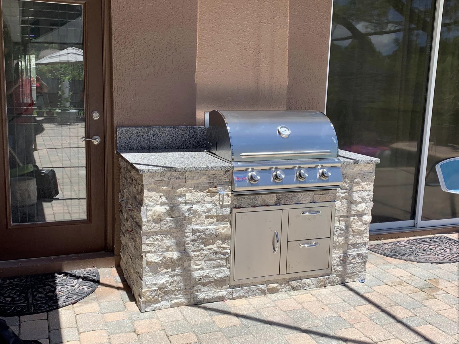 Stacked-stone grill island with granite top on a paver patio