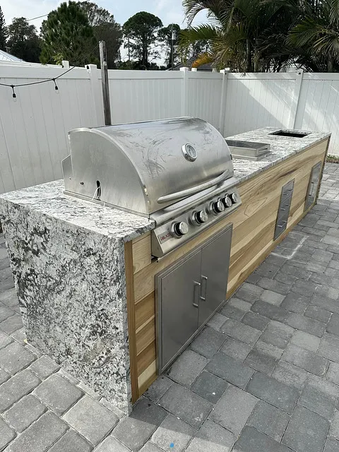 Granite and cedar grill island with stainless grill and storage doors on a paver patio
