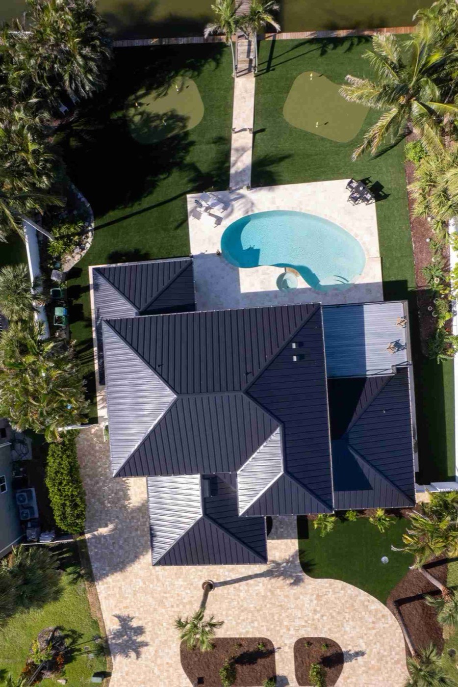 Overhead aerial of a kidney pool, travertine deck, turf lawn, and putting greens