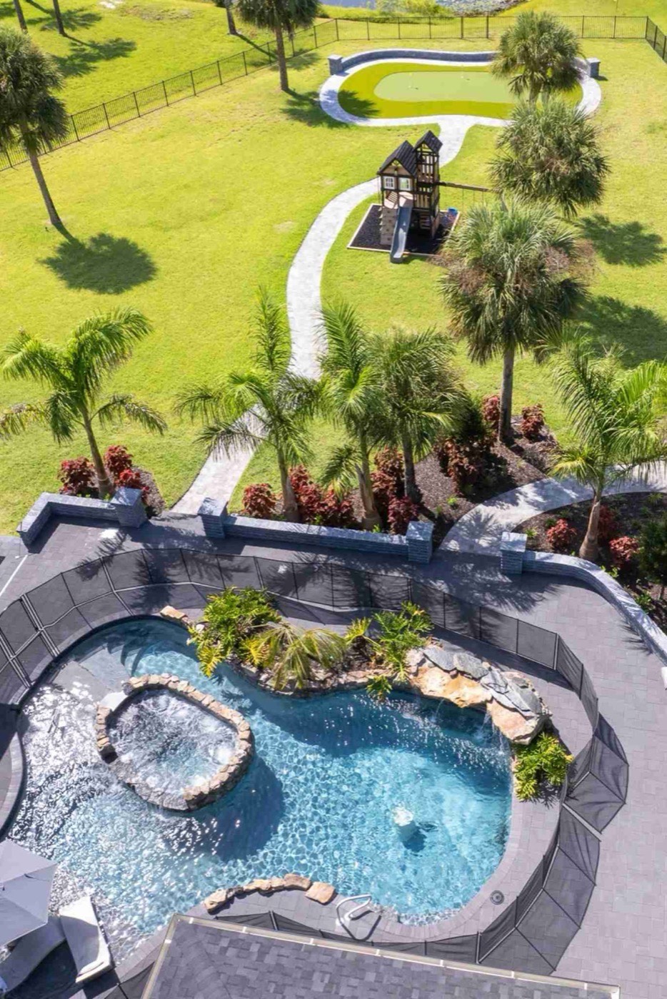 Aerial of a resort-style backyard with rock waterfall pool, playground, and putting green