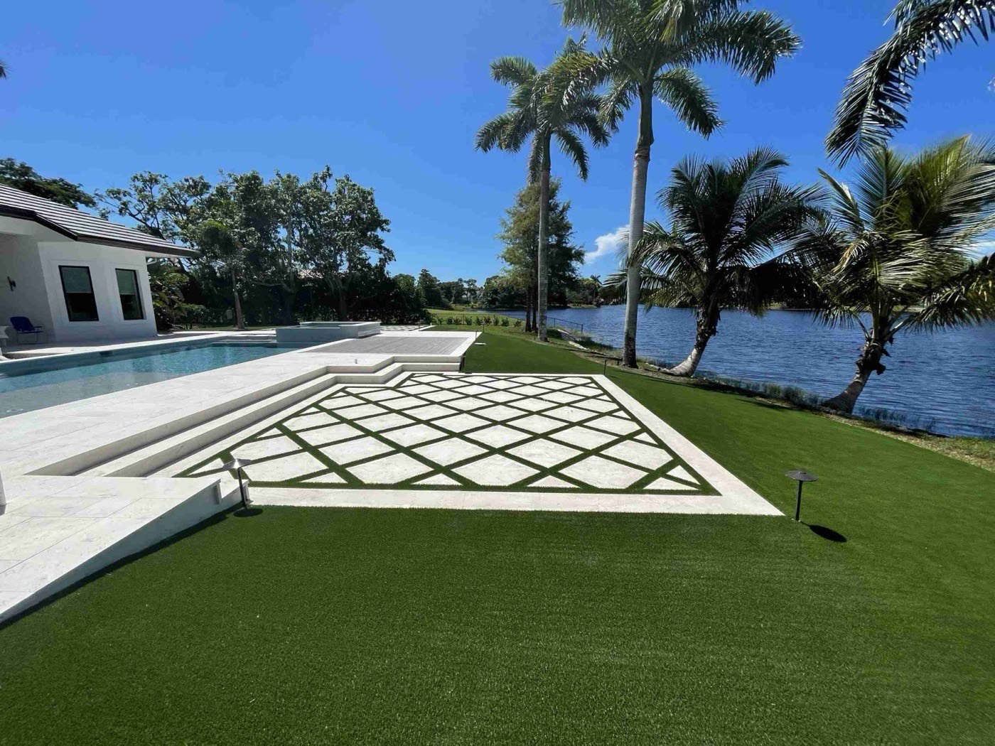Travertine and turf diamond-pattern patio between a pool deck and lake