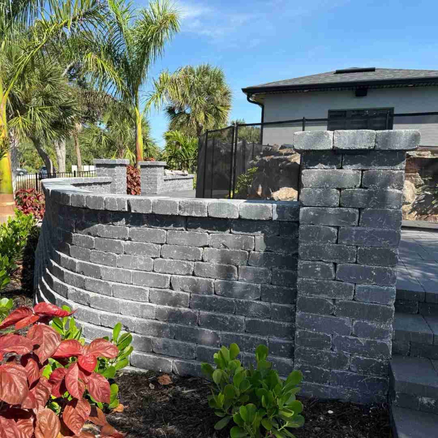 Curved charcoal block retaining wall with matching capstones beside a pool