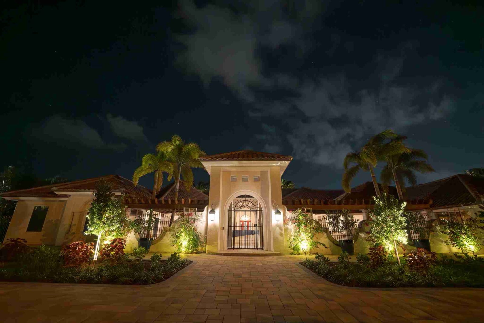 Paver entry courtyard and facade of a Mediterranean estate lit with landscape lighting at night