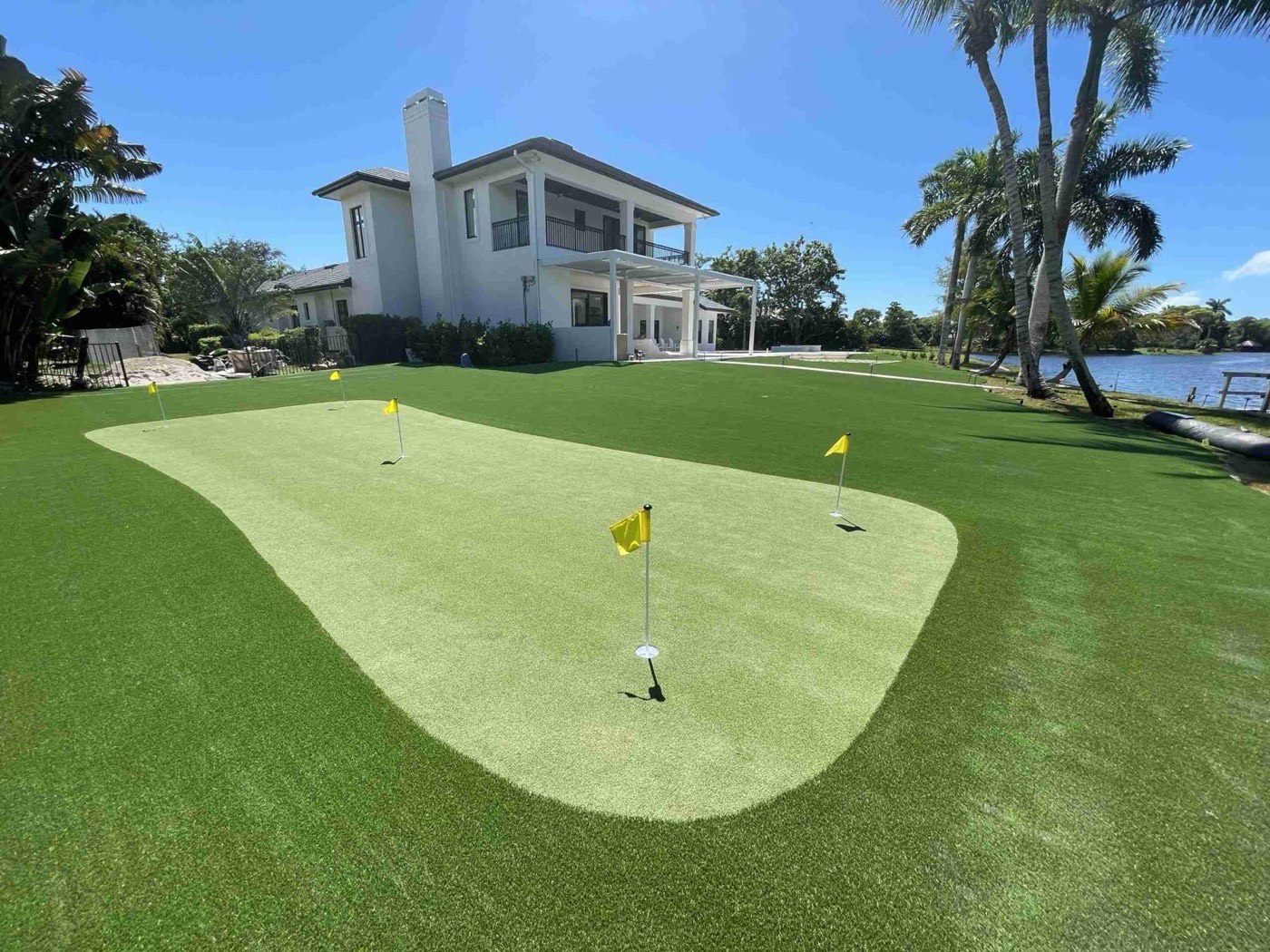 Lakefront synthetic turf lawn and putting green behind a modern two-story home